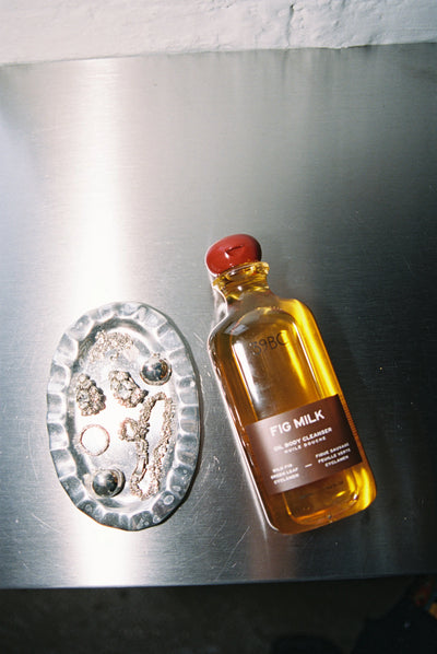 39BC Fig Milk Bath & Shower Oil on a metallic surface, styled with accessories